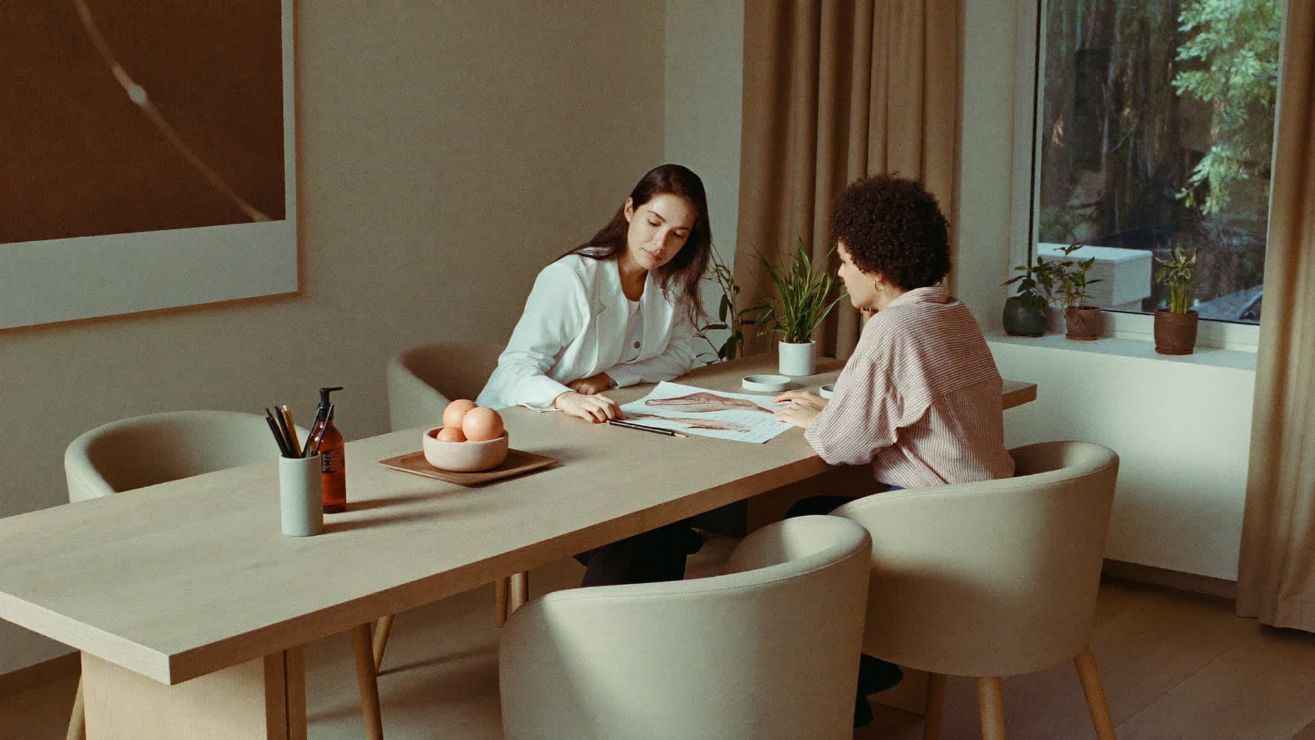 A practitioner and a client at a wooden table in warm morning light, reviewing a printed health panel together
